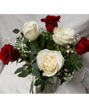 3 red and 3 white roses arranged in a vase With seasonal filler!