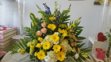 Bright l funeral Tribute Yellow, Gerbera's Yellow Snapdrogon, soft Peach Roses, and Blue Delphium.