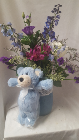 Boy Pearls and Lace Mason jar filled with shades  of blues, purples and whites and blue bear attached. Flower choices may vary depending on stock and seasonal.