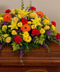 COLORFUL CONDOLENCES Half Casket Spray of gerbera daisies, lillies, carnations, roses, daisies,delphinium, and more. more.
