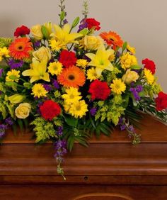 COLORFUL CONDOLENCES Half Casket Spray of  gerbera daisies, lillies, carnations, roses,  daisies,delphinium,   and more. more.