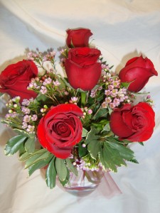 6 Red Roses arranged in a vase with baby's breath, Or wax flower whatever is in season .